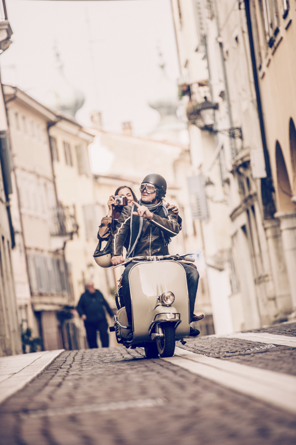 Vintage couple riding Vespa scooter in Italy, woman taking photos, front view