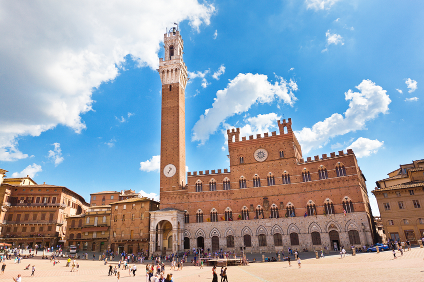 The Piazza del Campo, the public town square of the city of Siena, Tuscany, Italy, features the Palazzo Pubblico museum and its bell tower, the Torre del Mangia. The clam shell shaped piazza is a tourist destination, with street venders, restaurants, hotels, and retail shops. Horizontal cityscape with copy space.