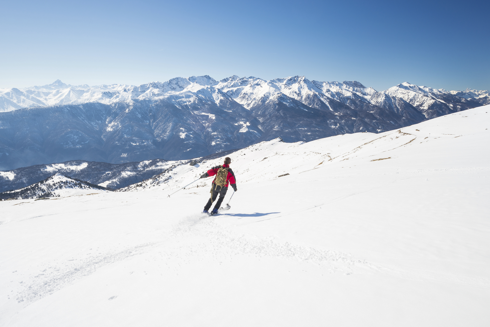 One person skiing downhills on snowy slope in scenic ski resort of the italian Alps, with bright sunny day of late winter season. Majestic mountain peaks in the background.
