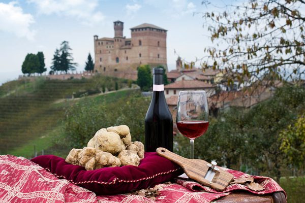 White truffles arranged on a pillow with wine and a shaver. a Piedmont landmark can be seen in the background