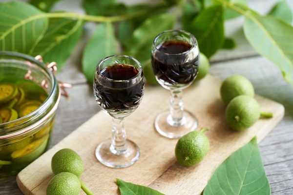 dark coloured walnut liqueur in glasses, surrounded by green walnuts
