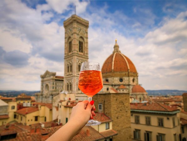 Hand with aperol Spritz and a view of the Duomo Cathedral in Florence, Italy