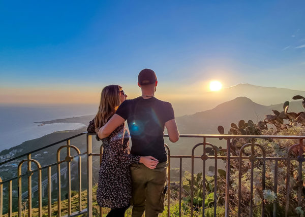 couple watching beautiful sunset behind volcano Mount Etna near Castelmola, Taormina, Italy
