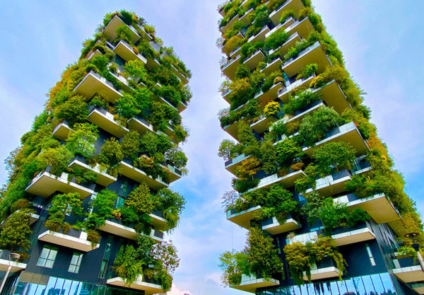 Two towering apartment buildings with balconies bursting with leafy trees