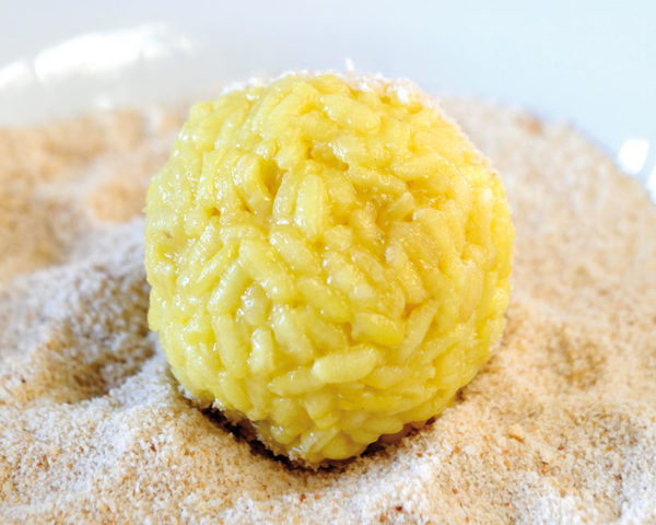 Uncooked rice ball on plate of breadcrumbs, ready to be rolled.