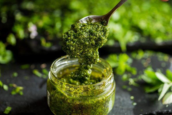 basil pesto being spooned from a jar