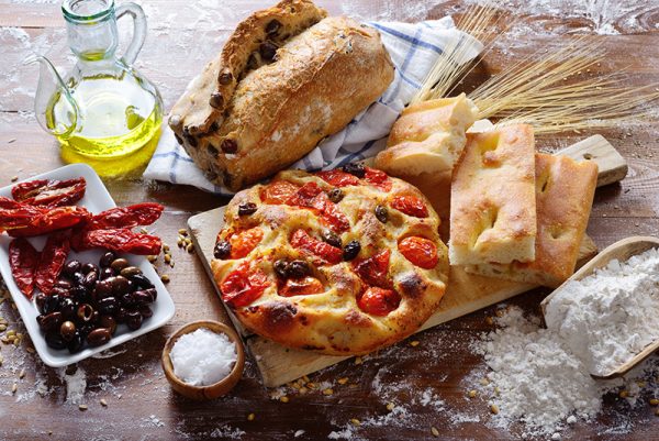 Focaccia on floured surface with tomatoes and olives