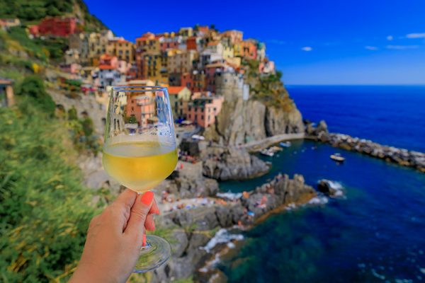 Woman's hand holding a glass of white wine, with Manarola, Cinque Terre in the background