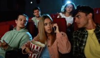 Young group in cinema being annoyed by woman on her phone