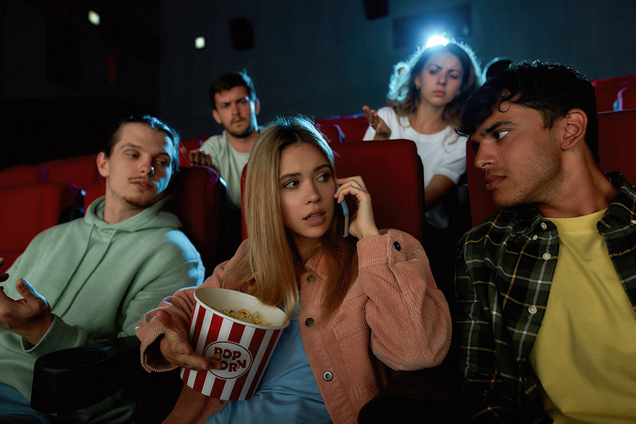Young group in cinema being annoyed by woman on her phone