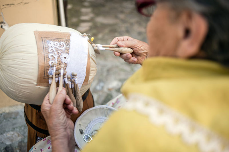 Elderly woman working on a "Merletto a tombolo" (Bobbin lace) in the street in front of her house in Offida