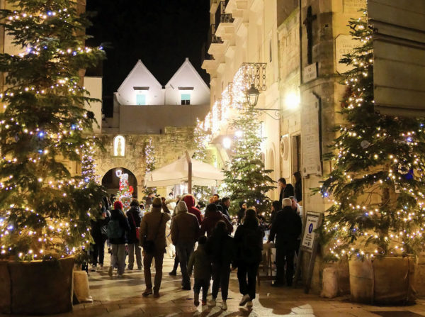Crowd walking through festive lit street with christmas trees