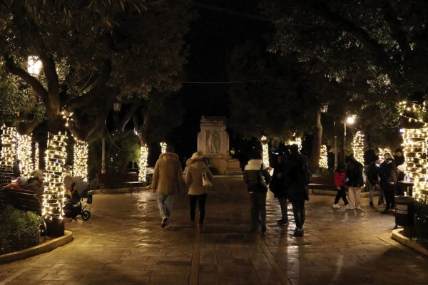 People walking in dark park. Lights are wrapped around trees to the side of the walkway, but the central area remains dark