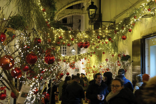 A crowd of people walking through Via Morelli after dark - with christmas decorations