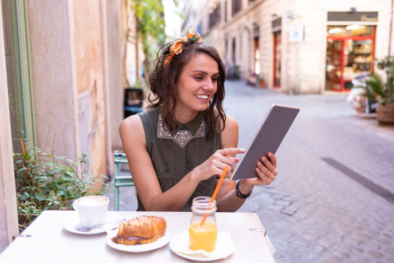 A woman using an iPad as she eats breakfast outside a cafe in Rome