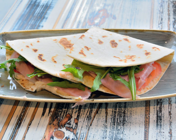 Piadina or Piada, thin Italian flatbread with smoked ham, rocket and ricotta cheese in San Marino