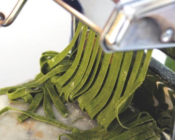 green spinach pasta cut into strips in pasta machine